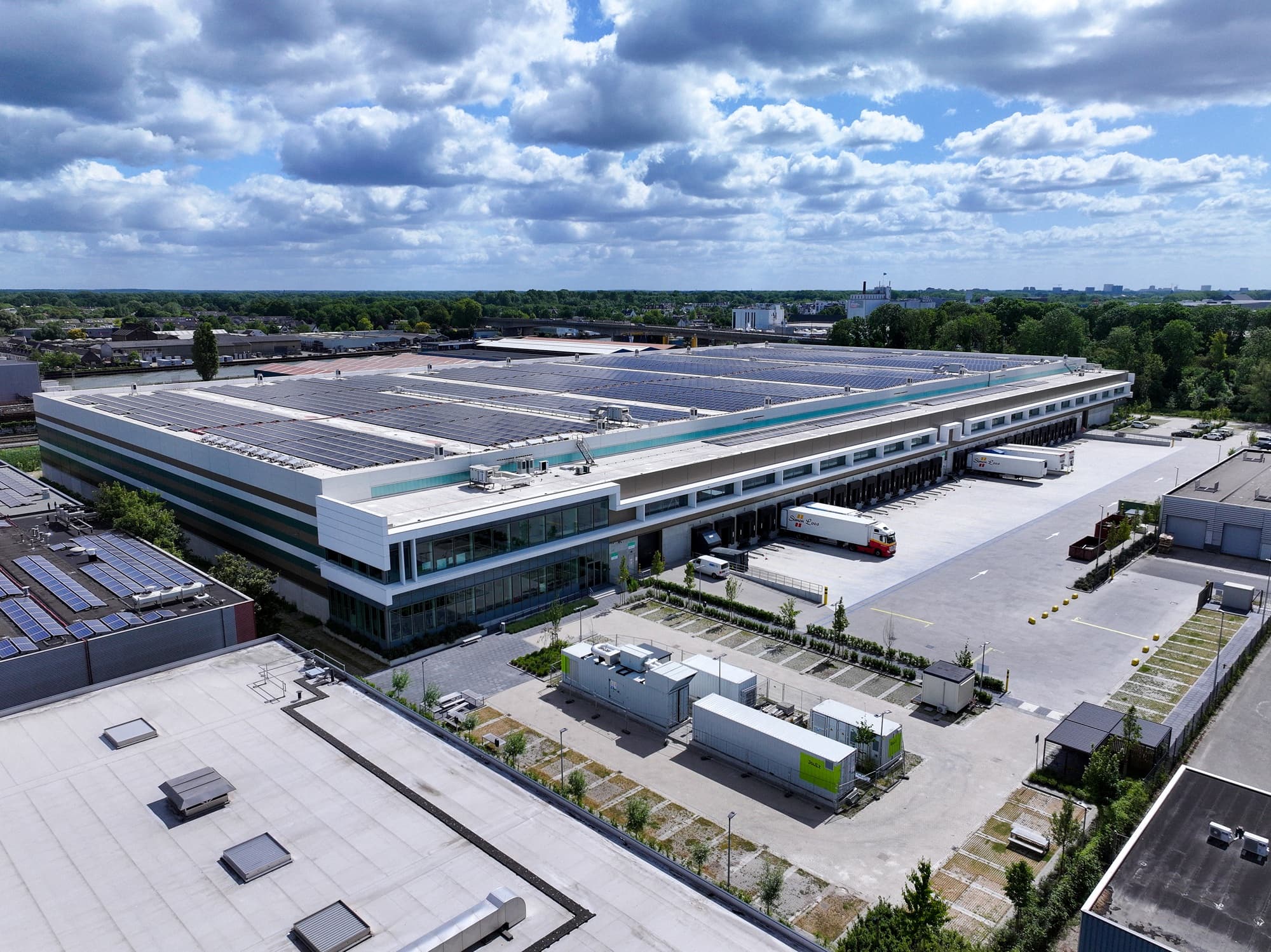 Distributiecentrum met zonnepanelen en microgrid energie-installatie, elektrische vrachtwagens onder bewolkte lucht